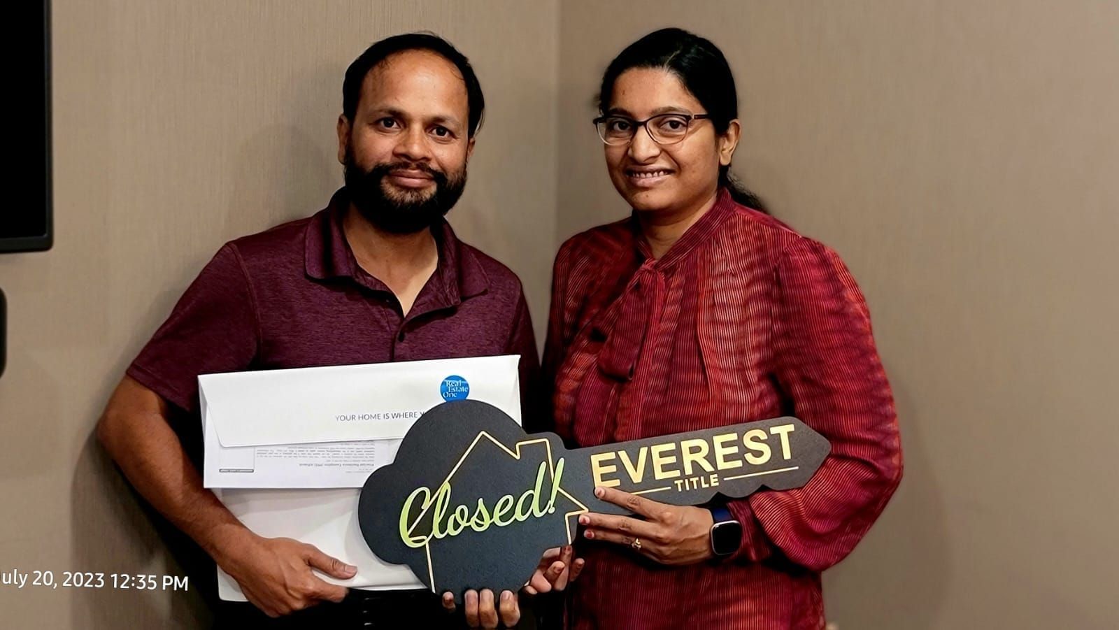 Two people smiling and holding a “Closed! EVEREST” sign against a plain wall.
