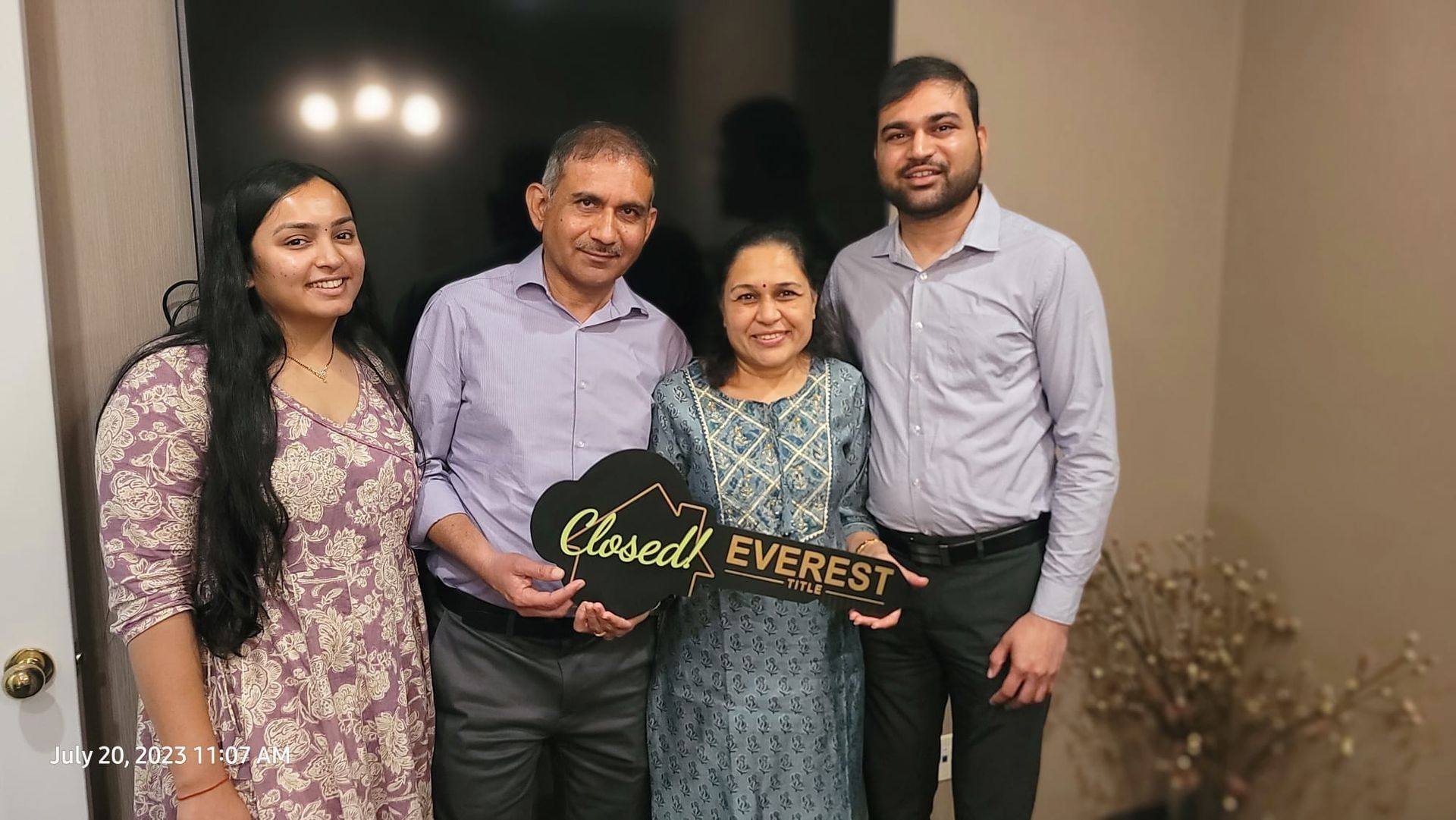 Four people indoors holding a gold-and-black “Happy Birthday” sign, smiling for a group photo.