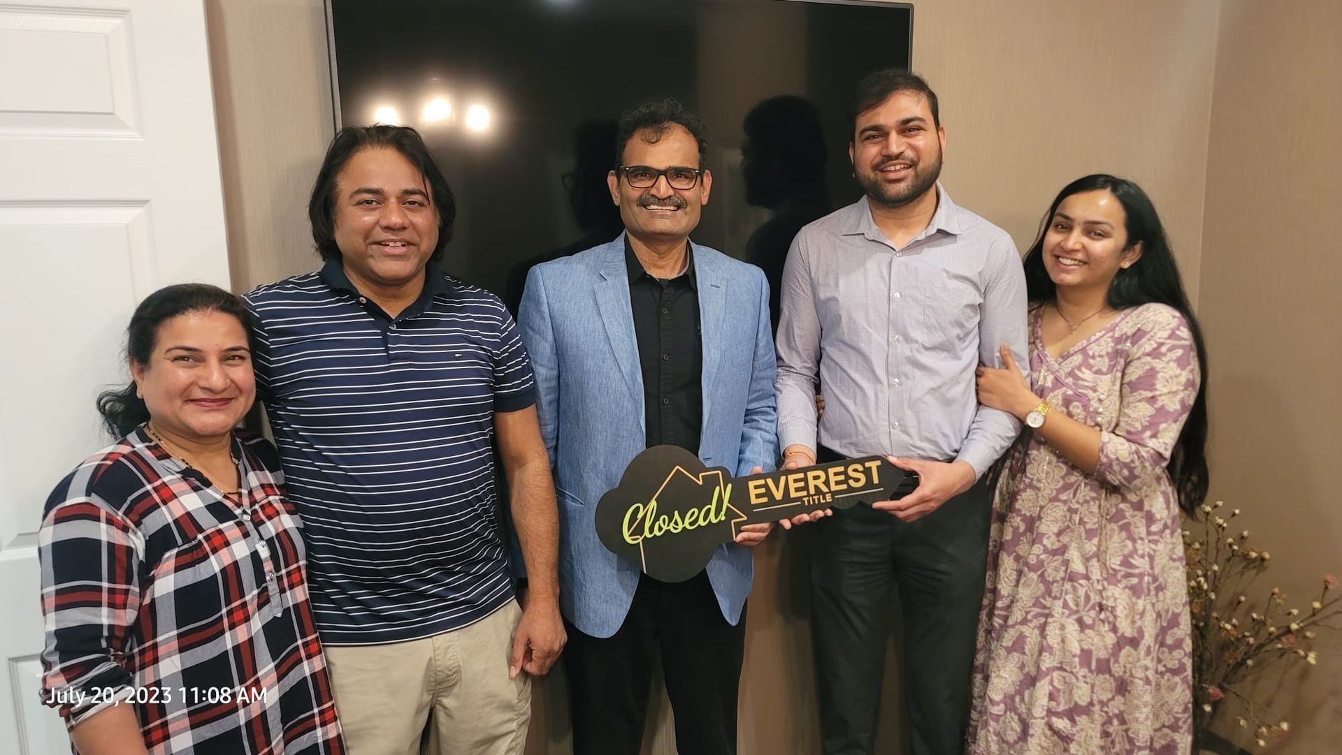 Five adults pose indoors, smiling, with one holding a “Congratulations Everest” sign.