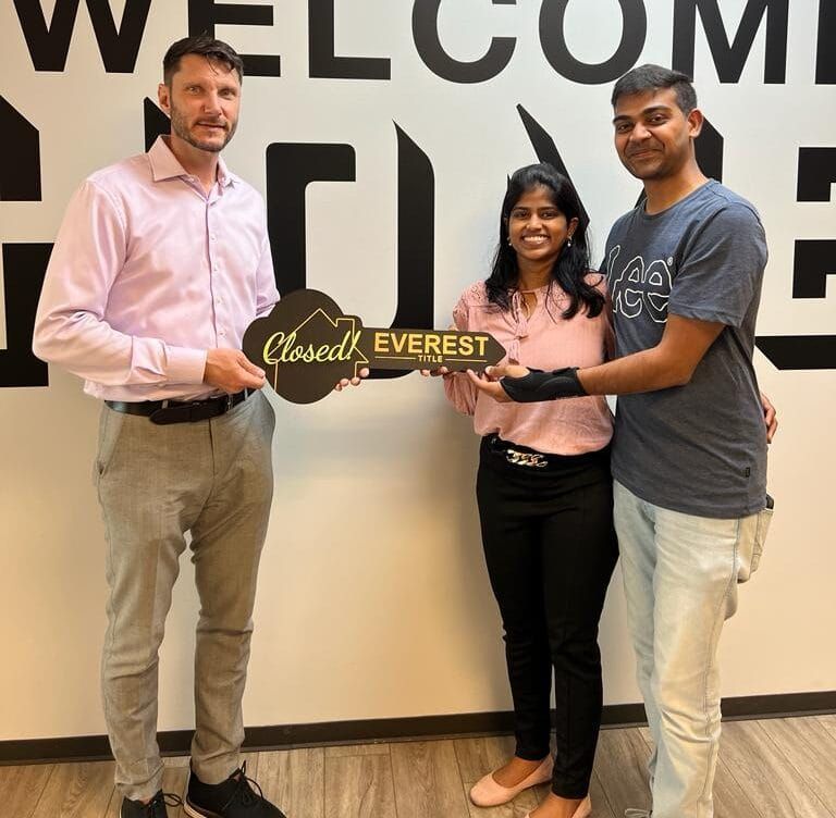 Three people holding a “Closed Everest” sign in front of a wall with large letters.