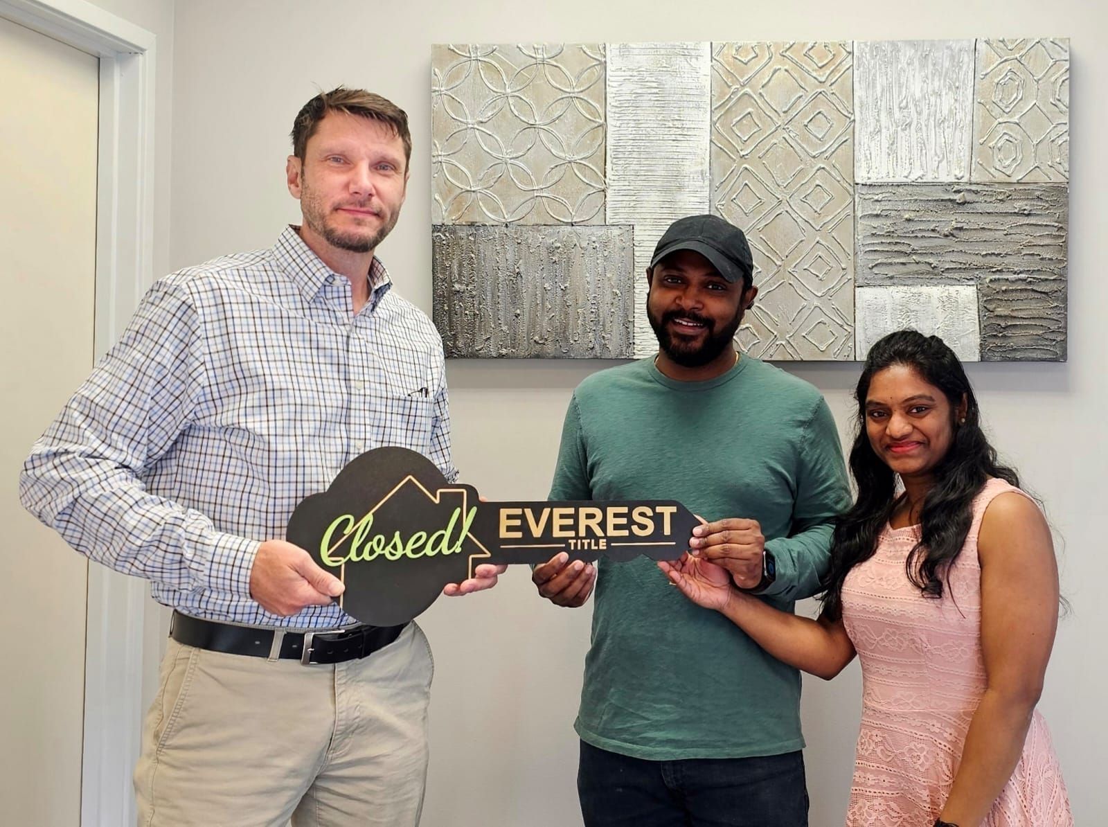 Three people in an office hold an “Opened EVEREST” key sign and smile at the camera.