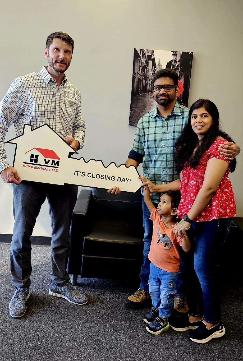 Three adults and a child holding a house-shaped sign in an indoor office setting.