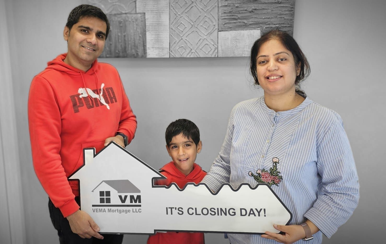 Family holding a house-shaped sign that says “IT’S CLOSING DAY!”