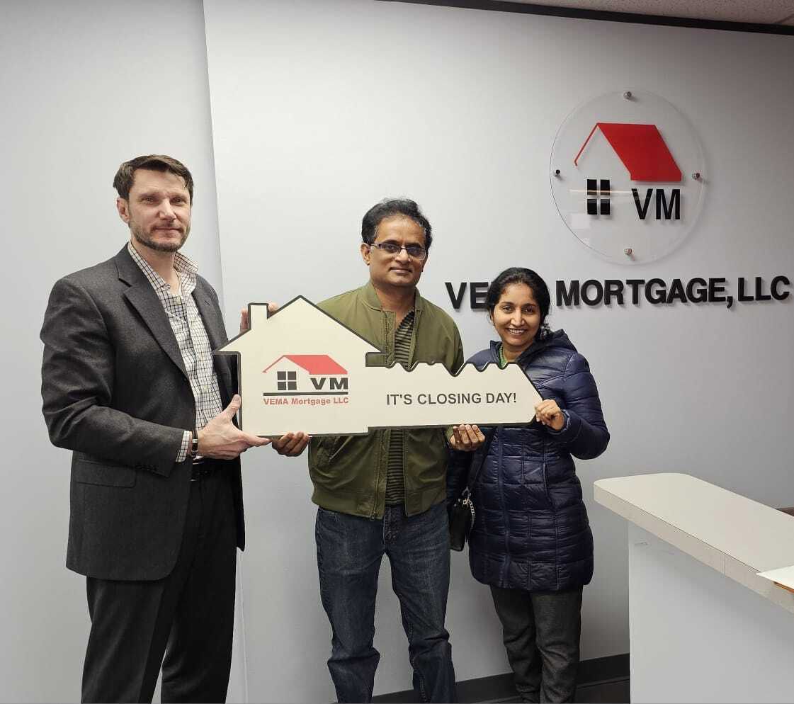 Three people holding a VM Mortgage LLC sign in an office lobby