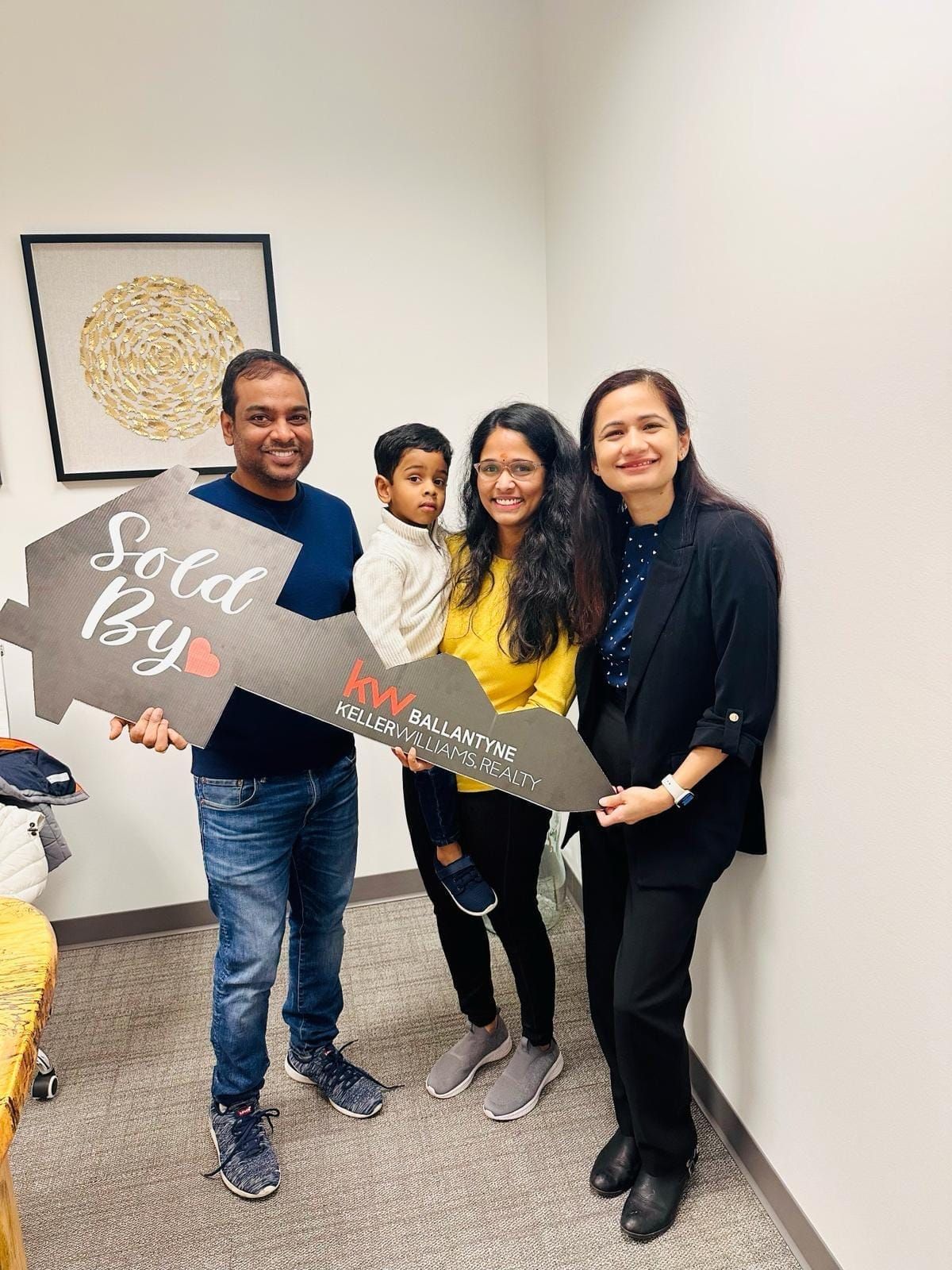Four people smiling and holding a large key prop in an office hallway.