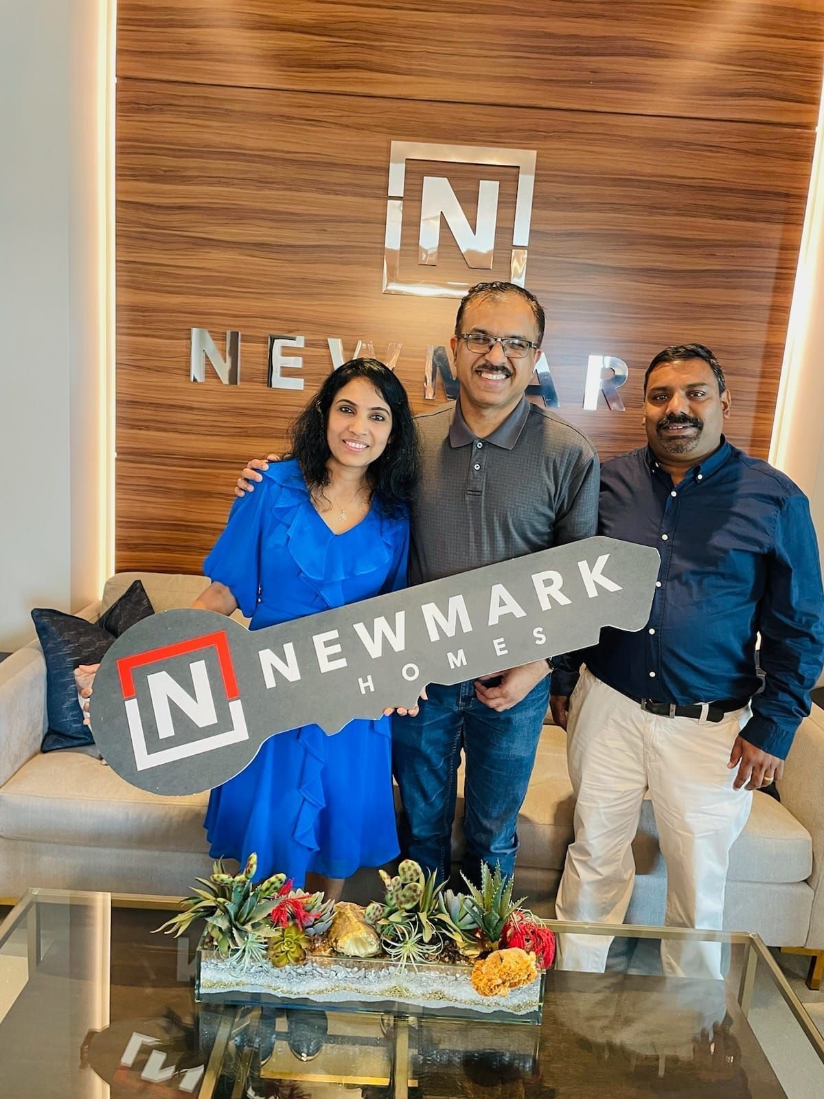 Three people posing with a Newmark sign in a modern office lounge area