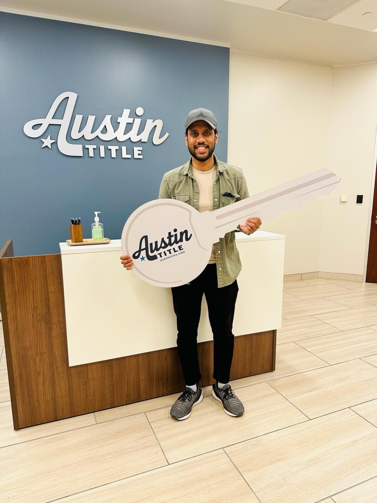 Man standing in an Austin Title office holding a large company sign, smiling at the front desk.