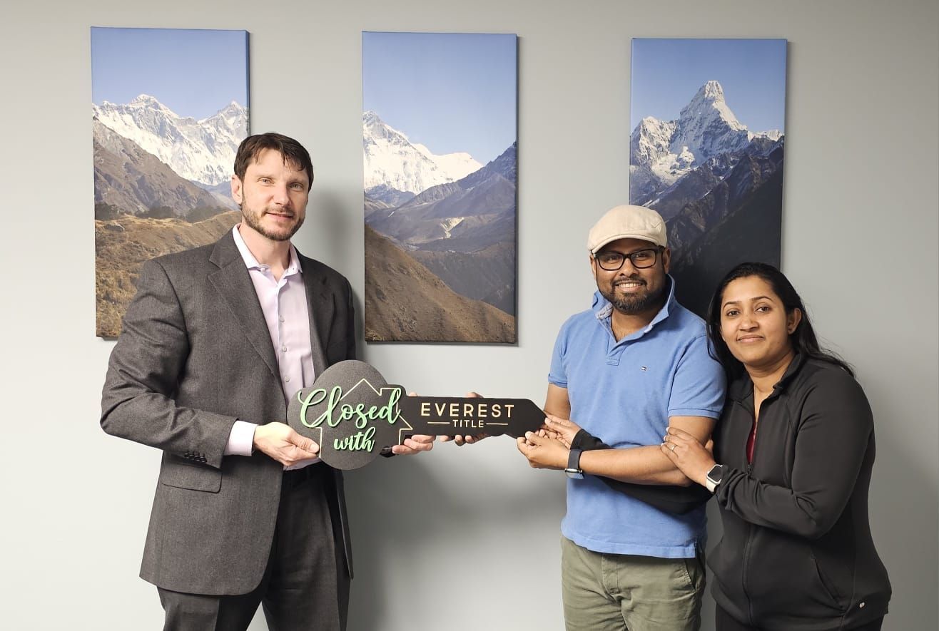 Three people hold a custom sign in an office with mountain landscape prints on the wall.