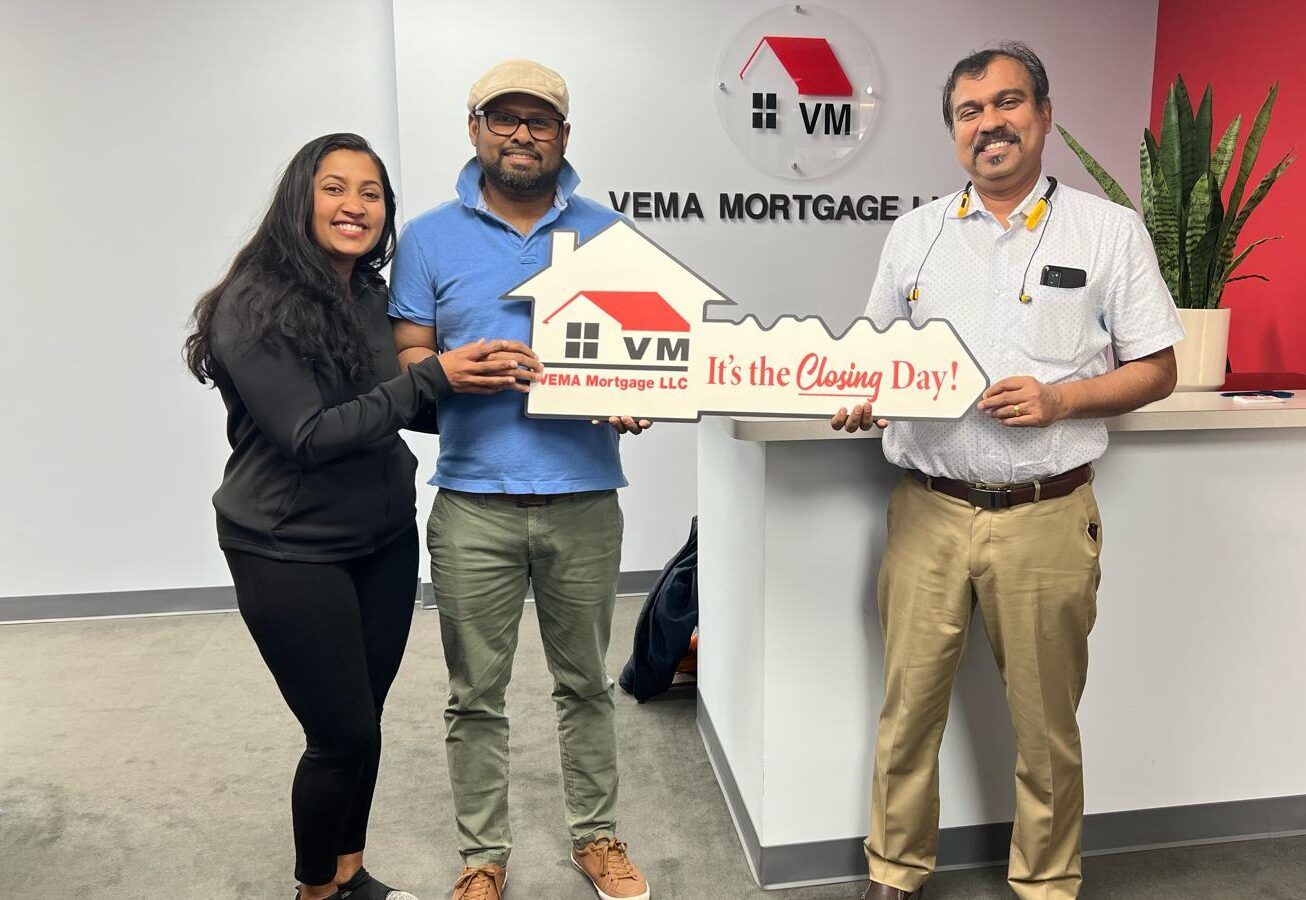 Three people posing at Vema Mortgage, holding a house model and a “It’s Closing Day!” sign