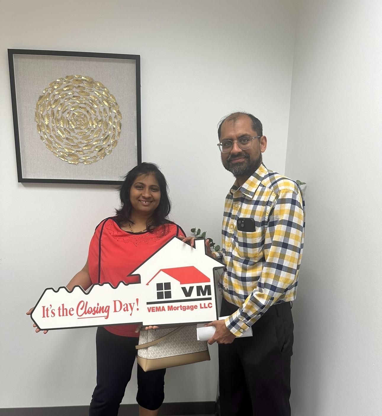 Two people holding a large decorative key in an indoor setting with a framed wall artwork behind them