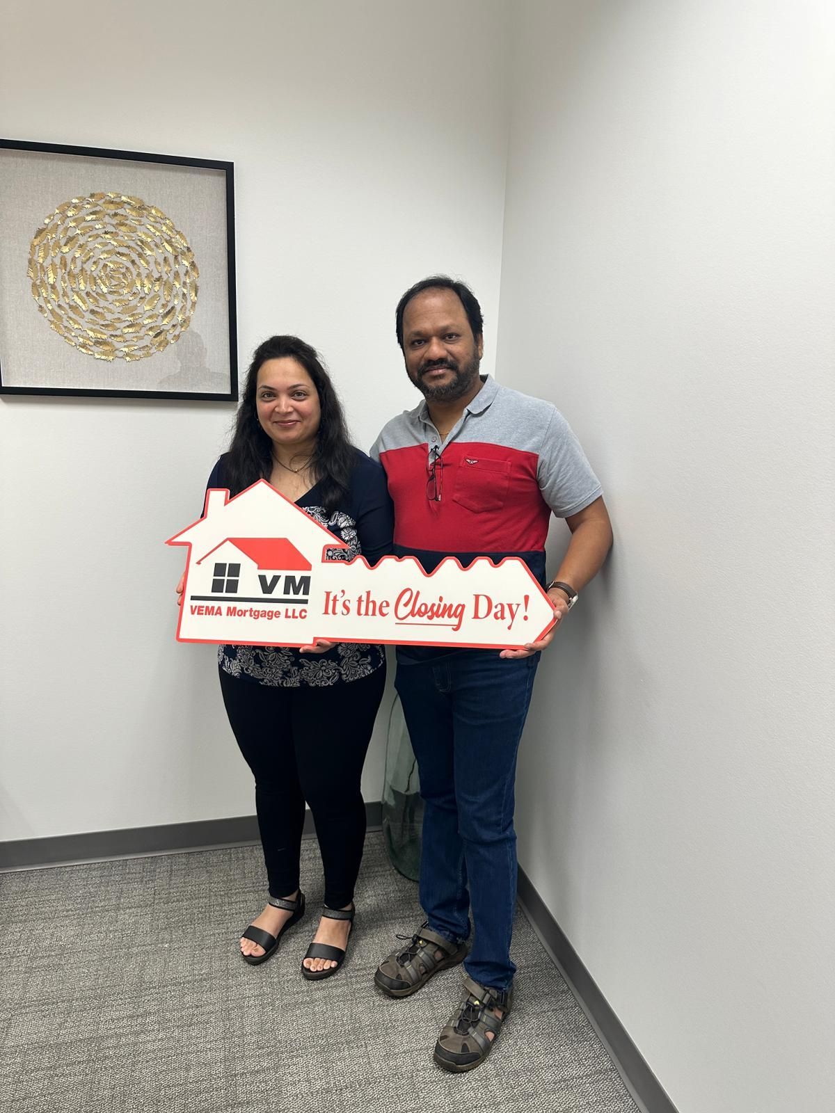 Two people holding a “Happy House Closing Day!” sign in an office hallway.