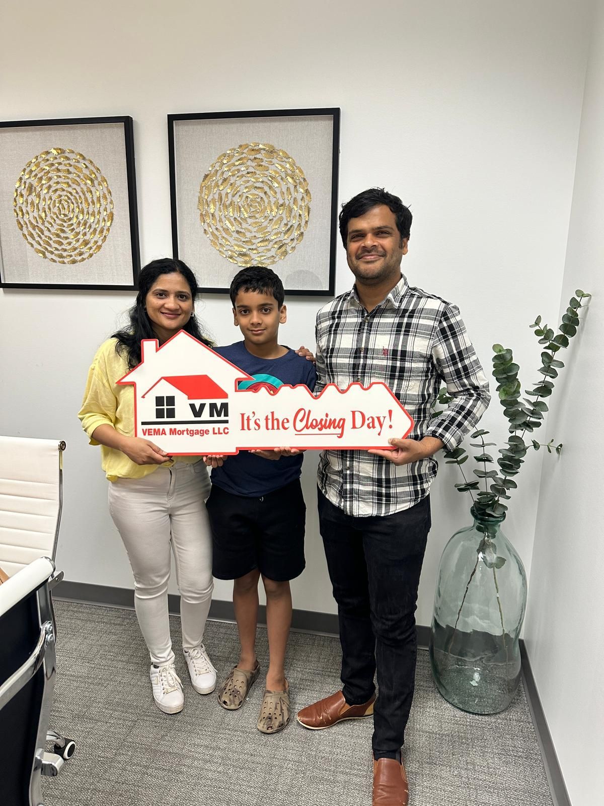 Three people hold a large orange “Happy Diwali” sign in a bright living room.