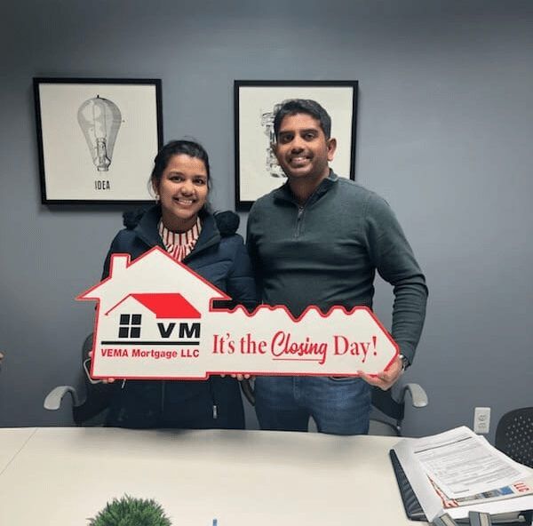 Two smiling people hold a “It’s the Closing Day!” sign in an office.