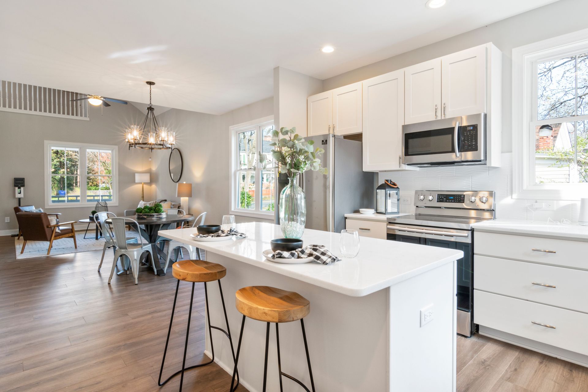 Bright modern kitchen with white cabinets, island stools, and open dining area in the background