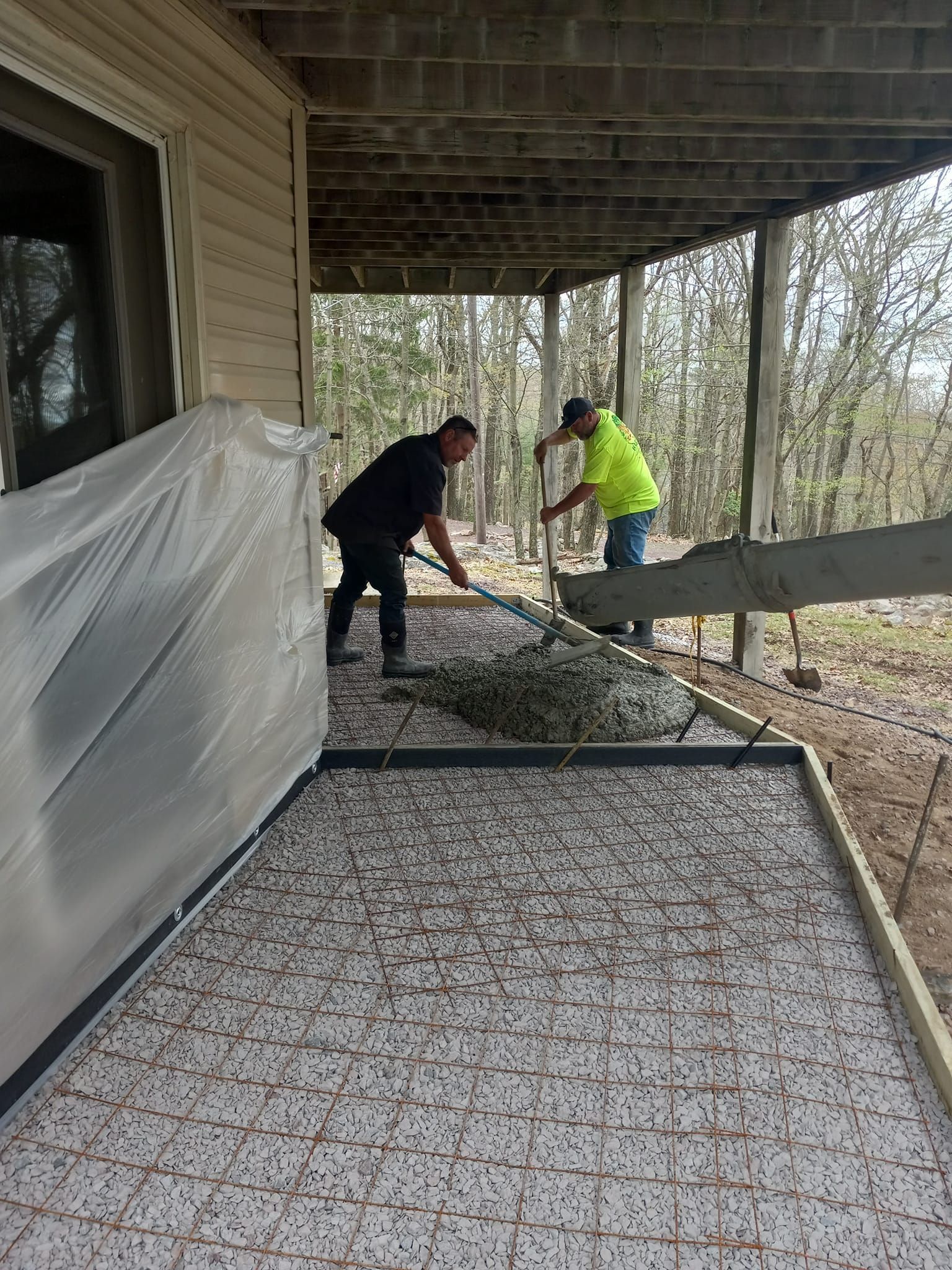Two men are working on a concrete patio under a porch.