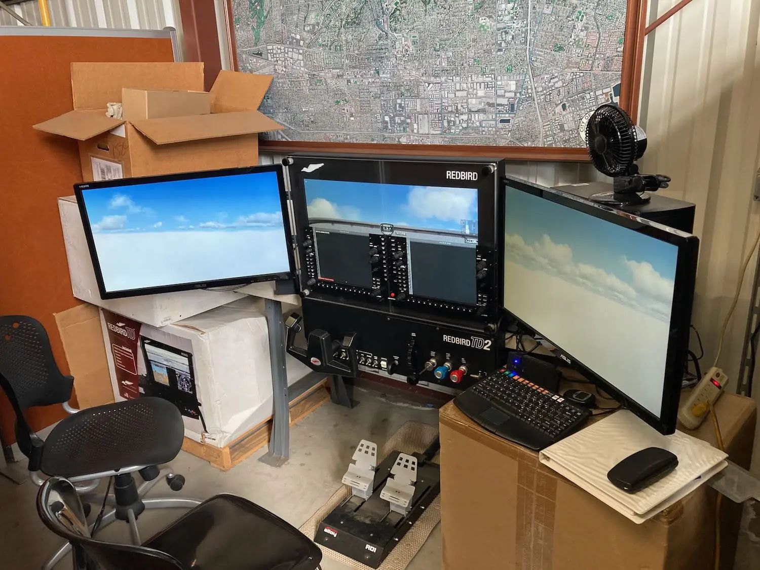 Multi-monitor desk setup in a cluttered workspace with computer equipment and boxes, one screen showing a beach scene