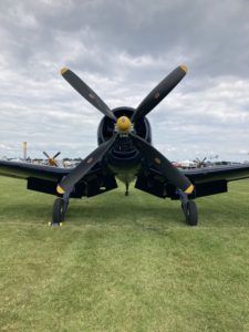 Vintage black fighter plane on grass, front view with propeller, under cloudy sky.