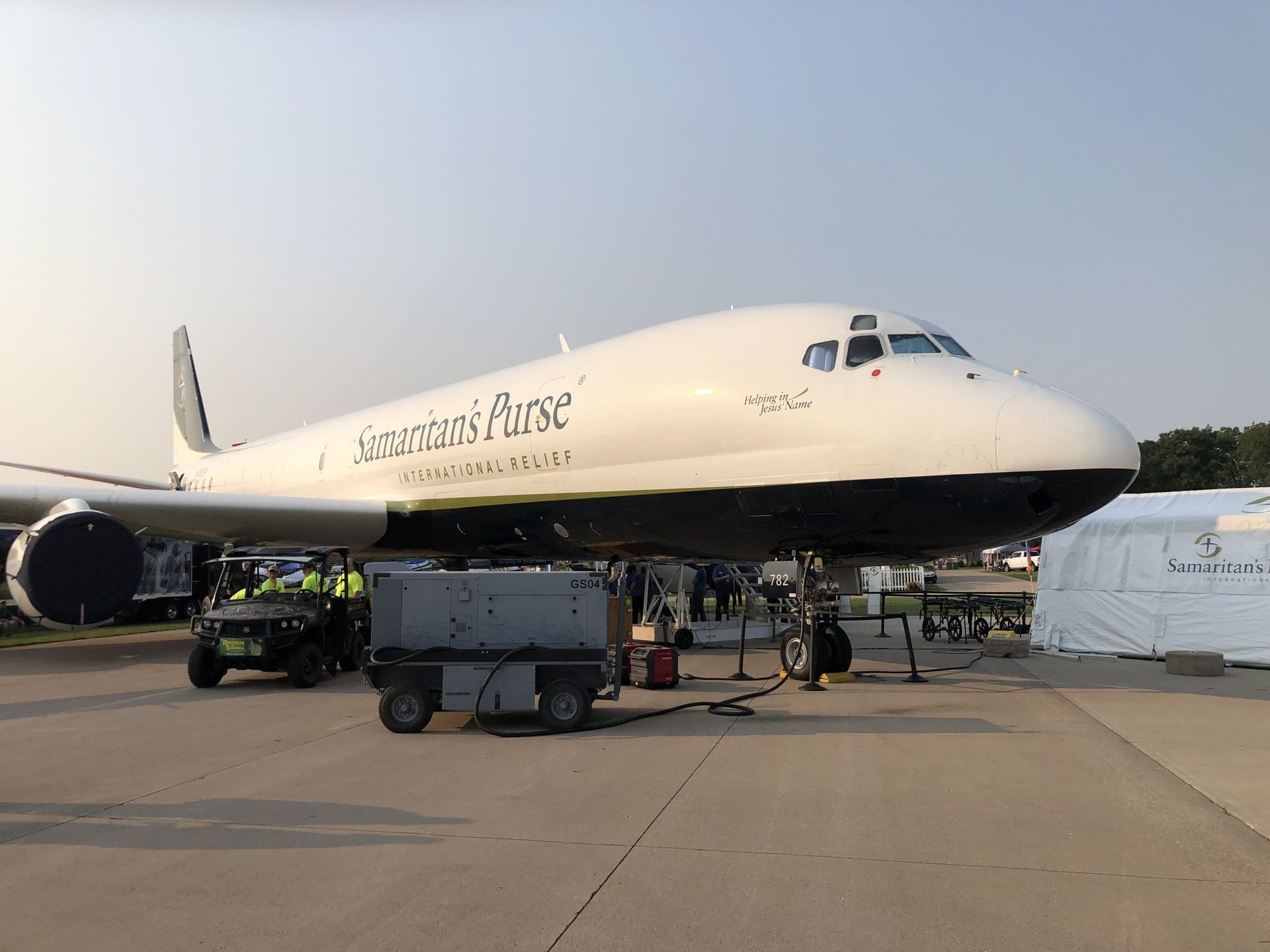 Large white airplane on tarmac with ground crew and service vehicles at sunset