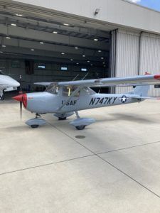 Small silver USAF aircraft parked outside a hangar, with red nose and tail number N747Y.