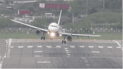 Commercial jet landing on a wet runway in rainy weather, headlights on.