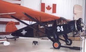 Black vintage airplane with number 24 displayed in a hangar, with a Canadian flag in the background
