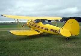 Yellow vintage biplane on grass airfield, side view with tail number G-WOCD