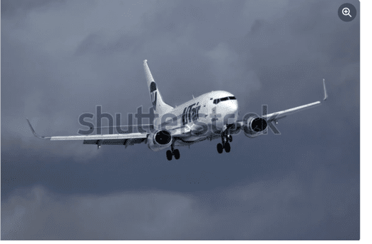 White commercial airplane descending in cloudy gray sky with landing gear down