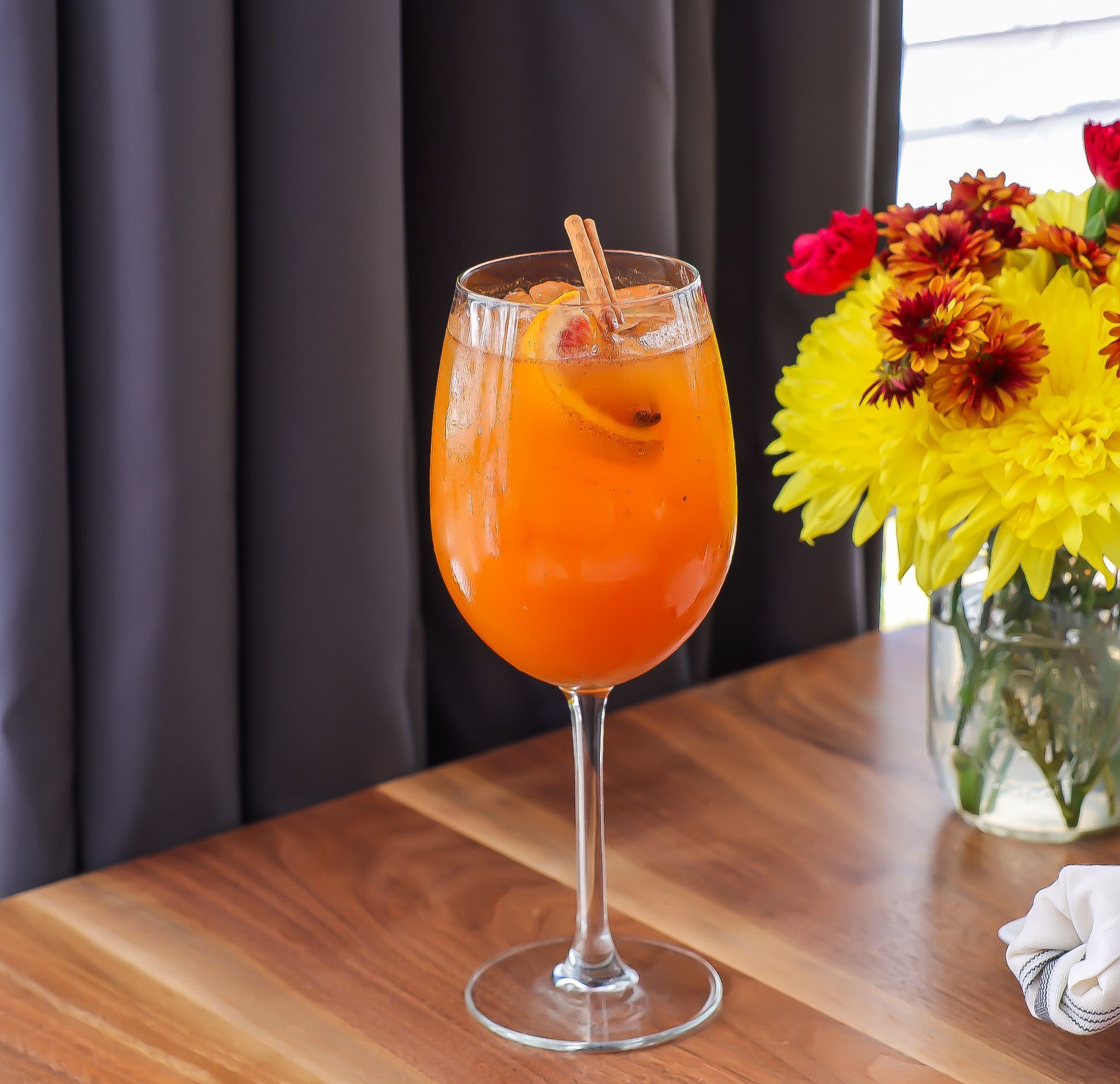 Orange cocktail in a tall glass garnished with cinnamon stick; table setting.