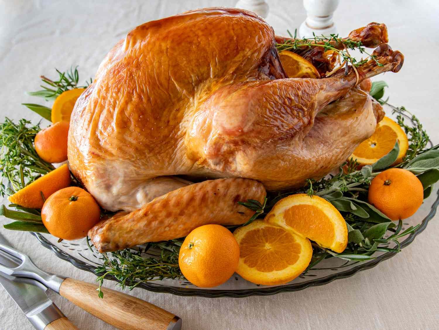 A turkey is sitting on a plate with oranges and herbs.