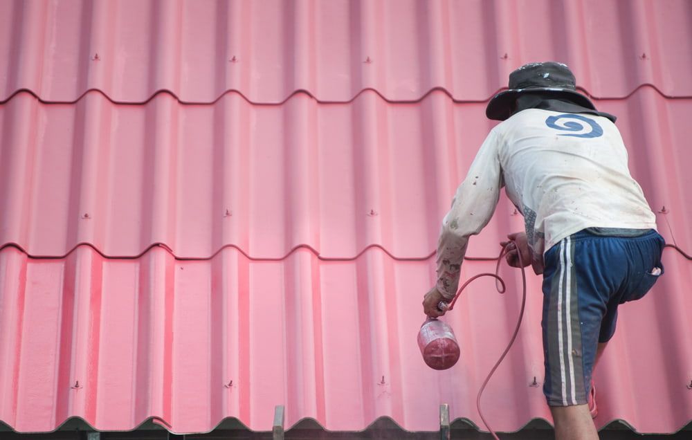 A Man Is Painting a Pink Roof with A Sprayer — Rooftech Roofing Services in Ballina, NSW