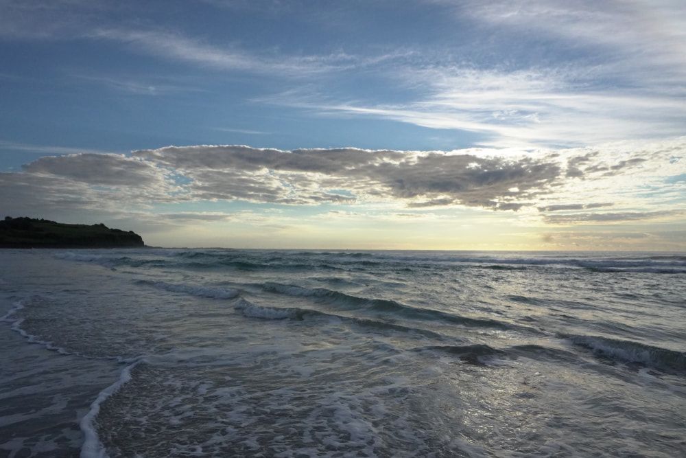 A Beach with Waves Crashing Against the Shore at Sunset — Rooftech Roofing Services in Ballina, NSW