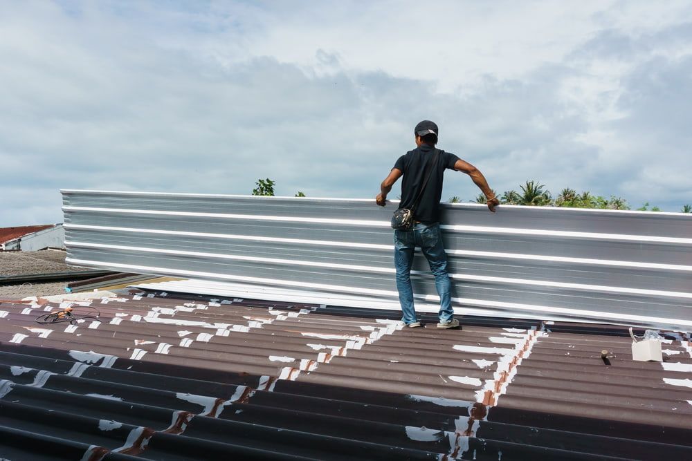 A Man Is Standing on Top of A Roof Holding a Piece of Metal — Rooftech Roofing Services in Casino, NSW