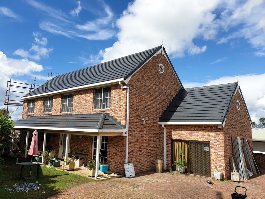A Large Brick House with A Black Roof and A Garage — Rooftech Roofing Services in Northern Rivers, NSW