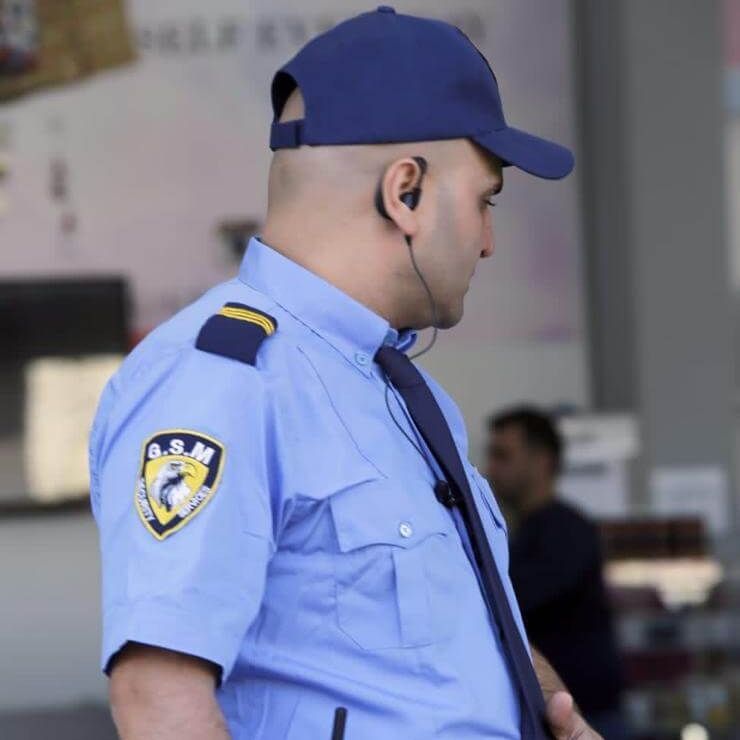 Professional security by GSM Facility Services Security guard wearing a blue uniform and cap, looking to the side, ear piece visible.