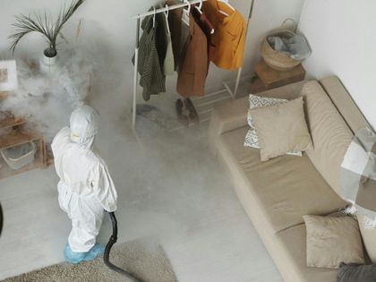 Person in hazmat suit disinfecting a room, fog engulfing the space.