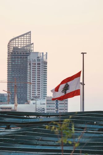 Lebanese flag waving against a backdrop of tall buildings and a light sky.