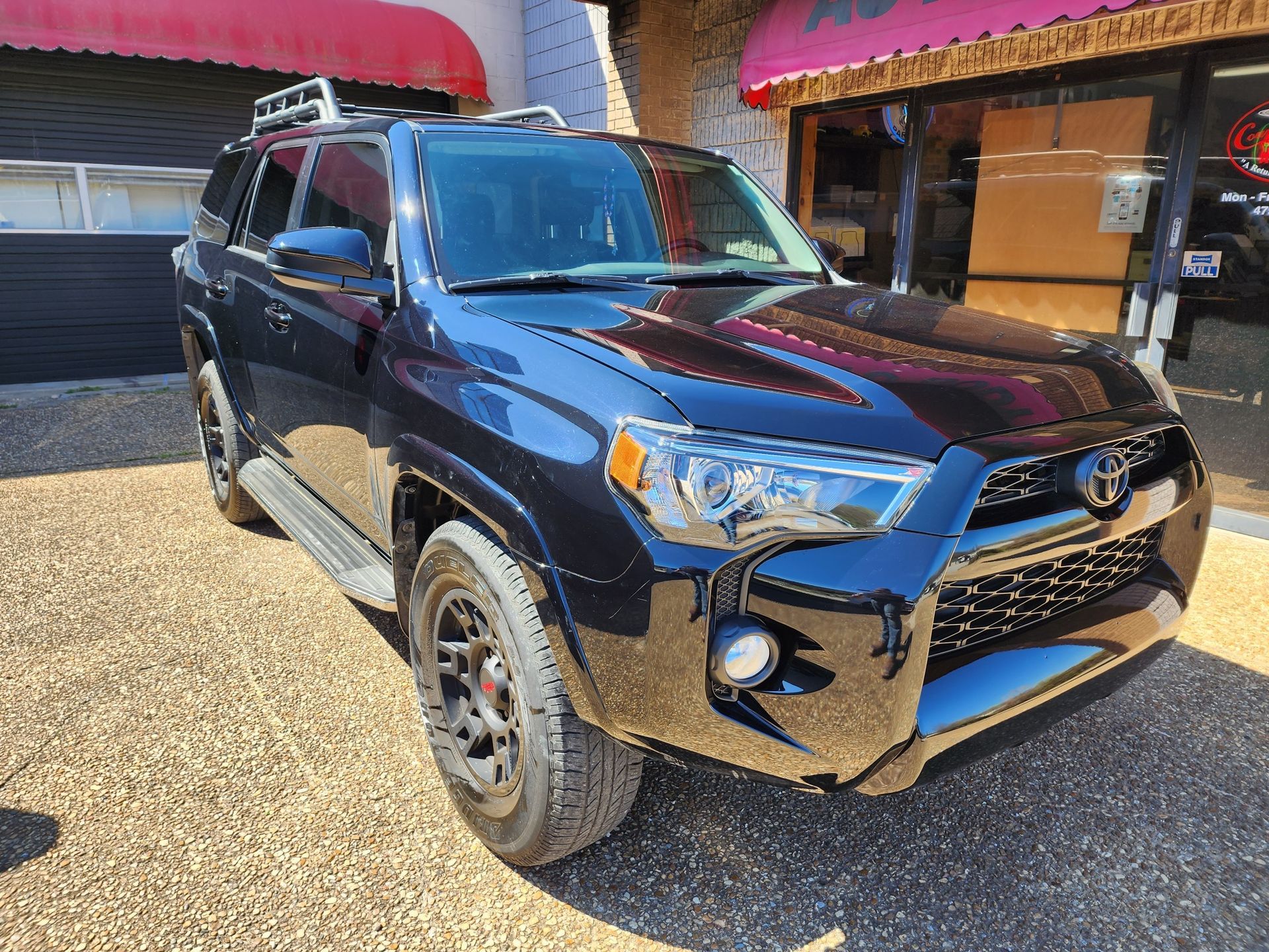 Black Toyota 4Runner parked in front of a building with red awning.