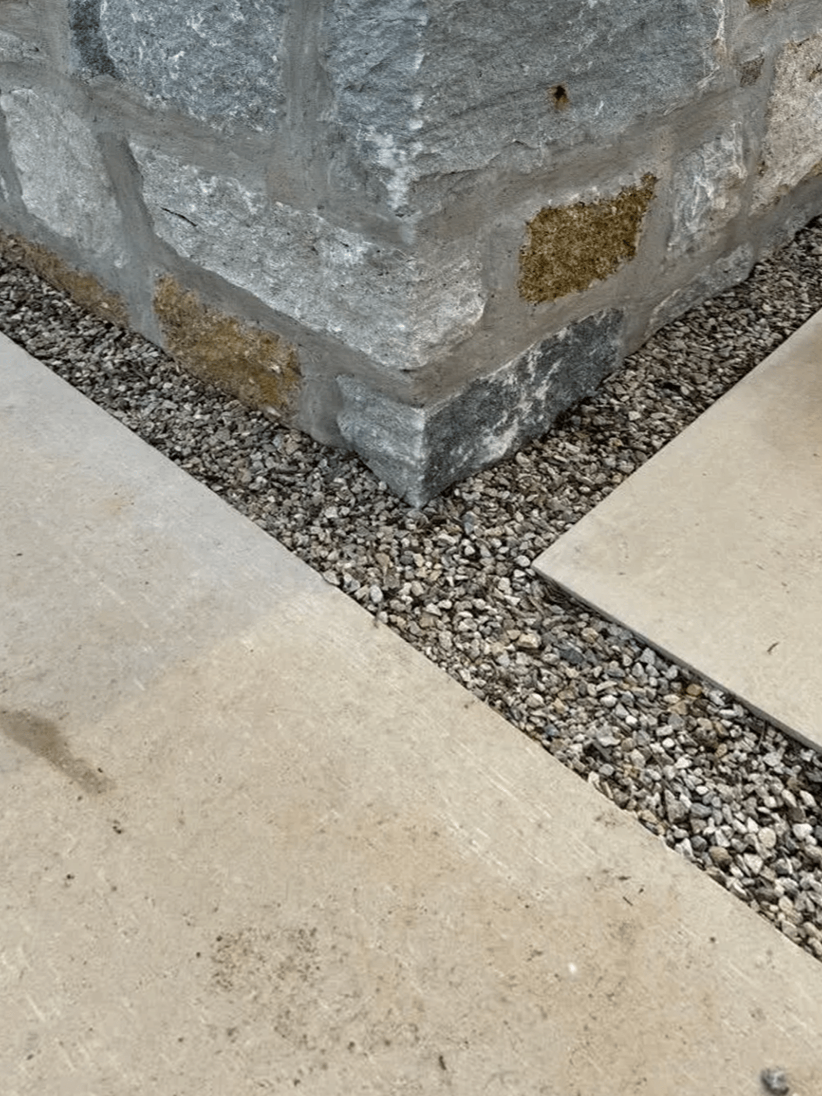 Stone wall corner, gravel, and light-colored paving stones.