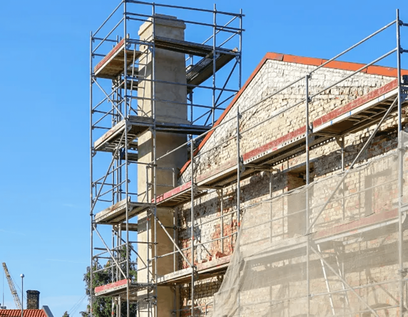 Scaffolding surrounds a building's brick facade and chimney during a renovation project.