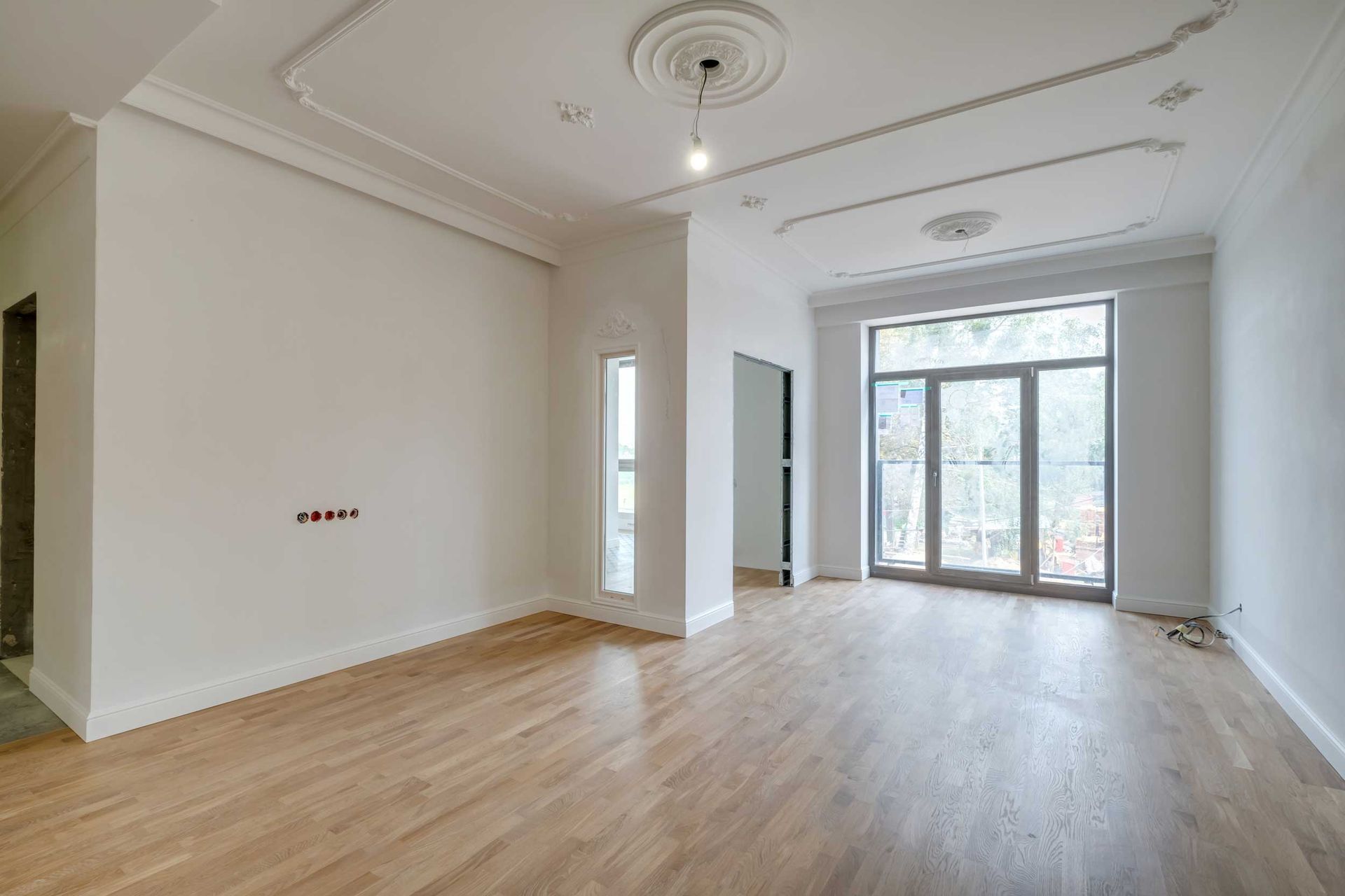 Empty modern living room with light wood floors, white walls, and large windows opening to a balcony. Empty modern living room with light wood floors, white walls, and large windows opening to a balcony.