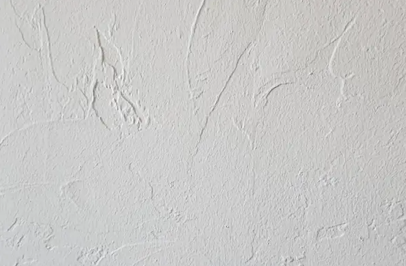White textured stucco wall with subtle cracks and uneven plaster patterns