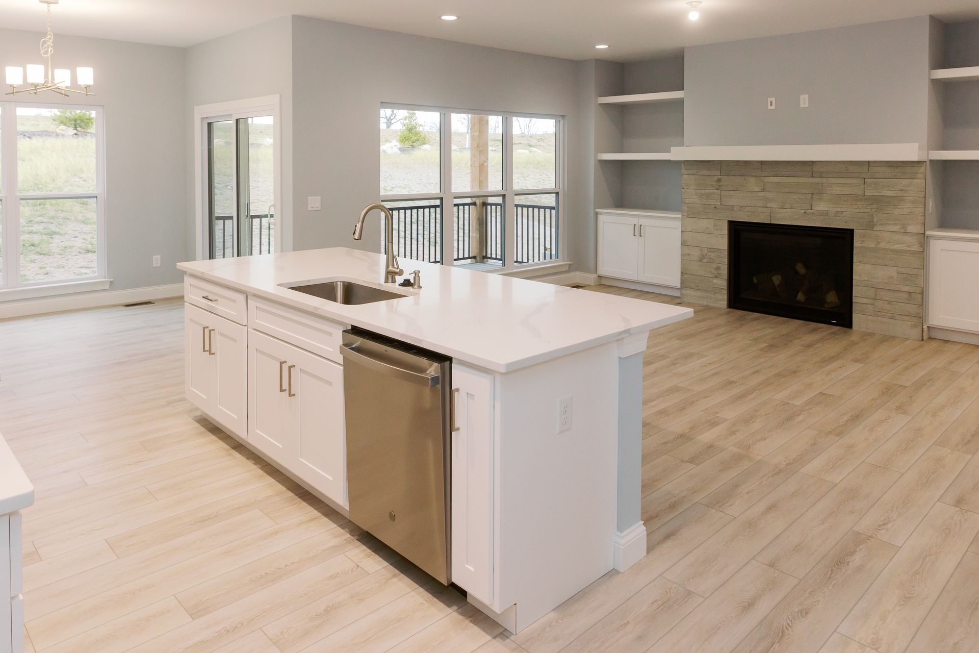 Modern kitchen of the Dean Martin model with white island, stainless steel appliances, fireplace, and light wood flooring.