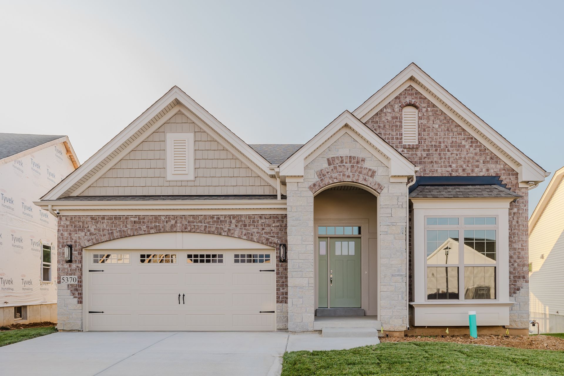 Exterior view of the Humphrey Bogart model with brick and tan siding, garage, and green door.