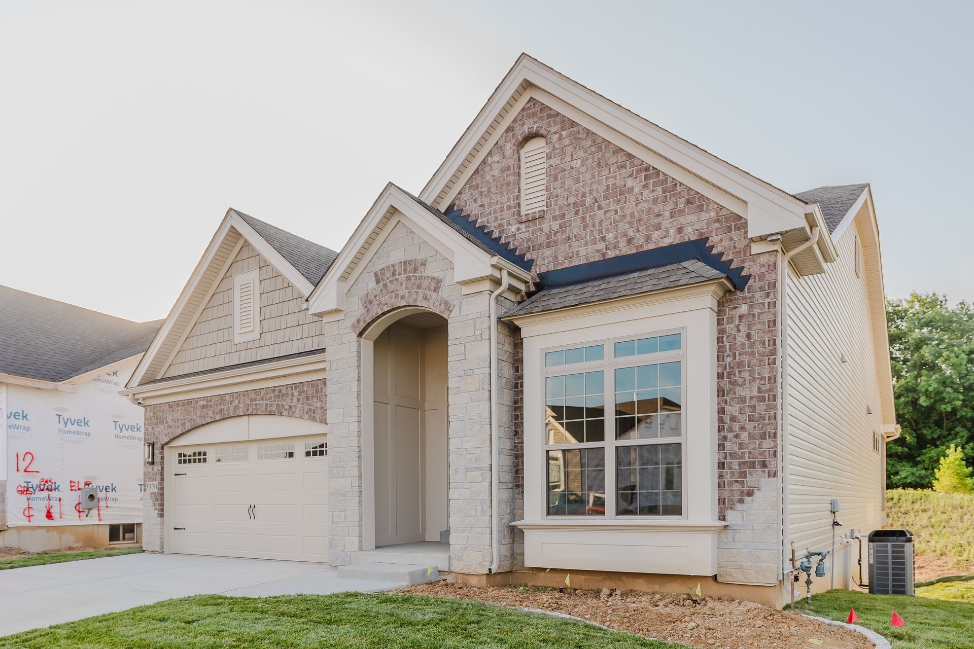 Exterior of the Humphrey Bogart model showing a garage and arched entryway, a bay window, and a green lawn.