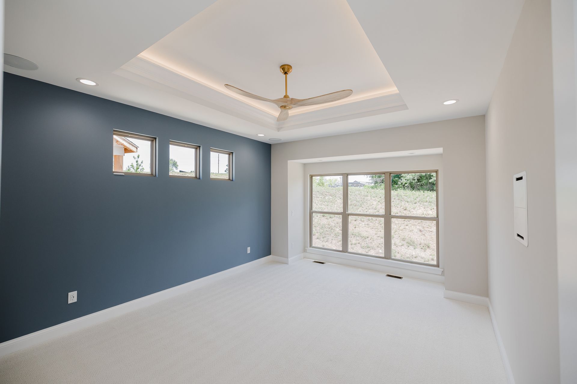 Spacious master bedroom of the Humphrey Bogart model with a blue accent wall, white carpet, and a decorative ceiling.