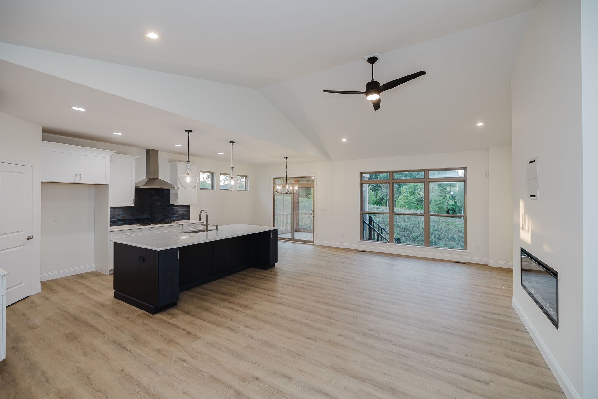 Open-concept kitchen of the Marilyn Monroe model and living area with a dark island, large windows, and a vaulted ceiling.