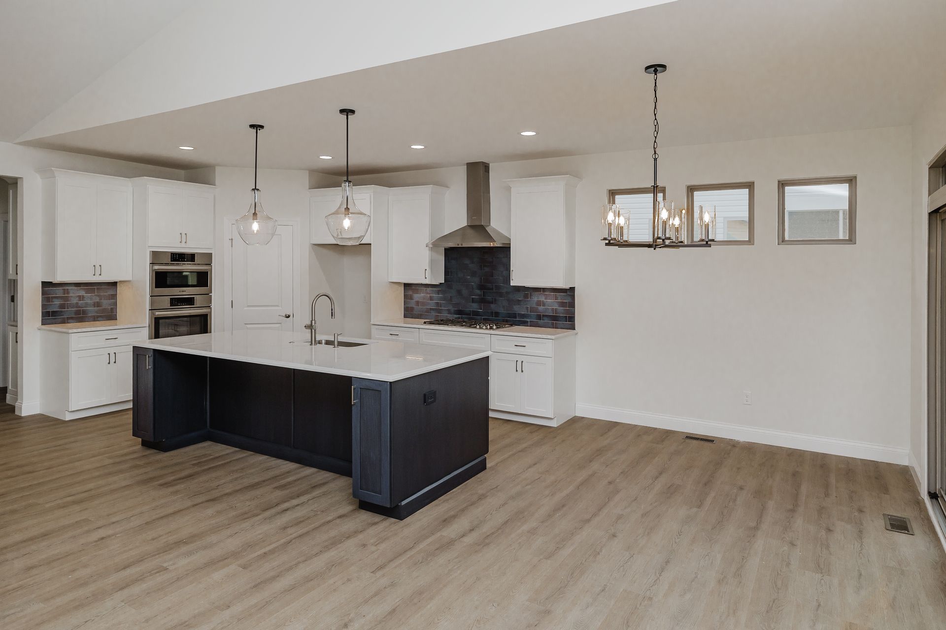 Modern kitchen of the Marilyn Monroe model with white cabinets, dark island, stainless steel appliances, and wood floors.