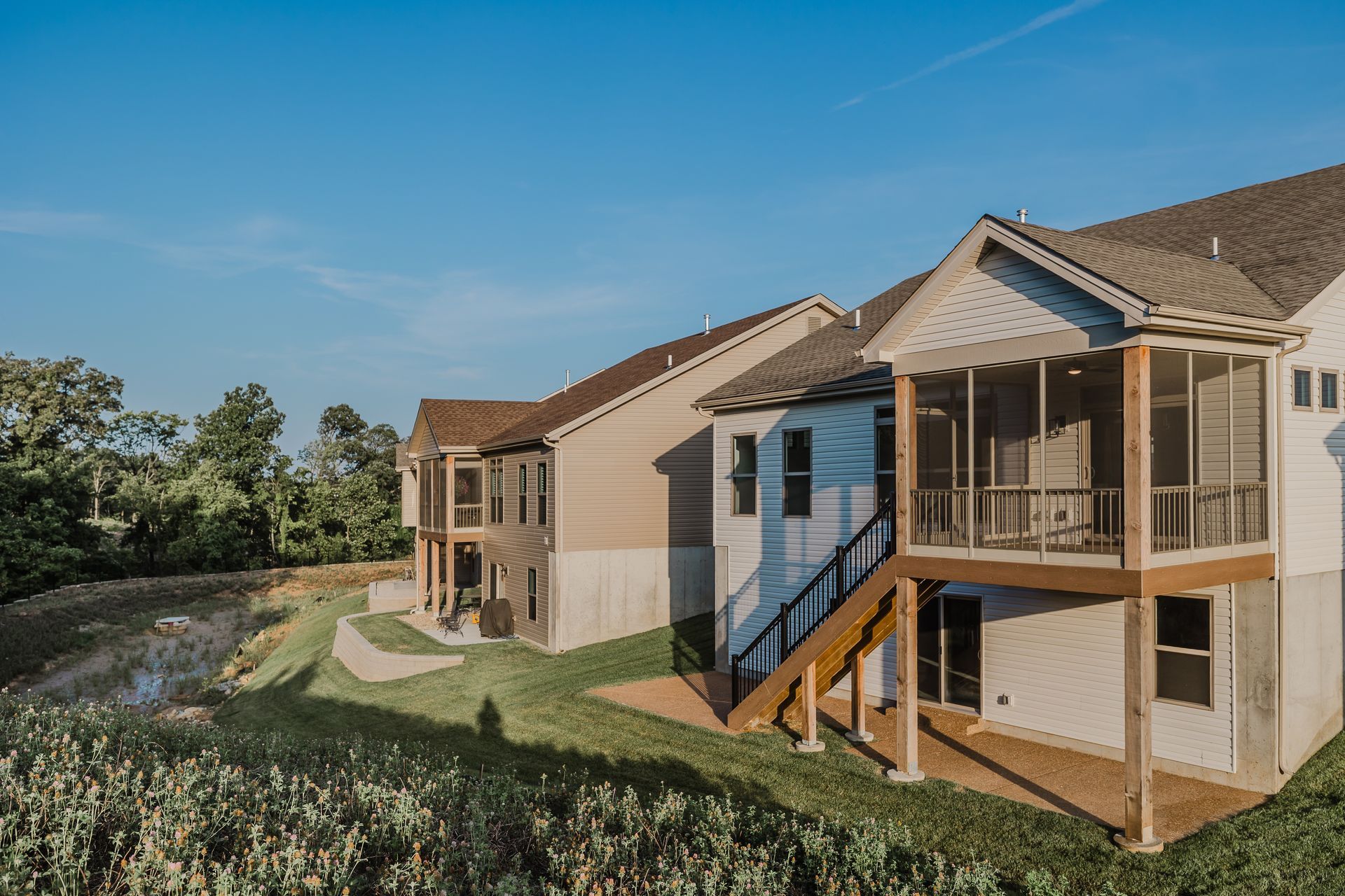 Two-story Marilyn Monroe model with screened porch, deck, and pond. Beige and gray siding, brown roof, blue sky.