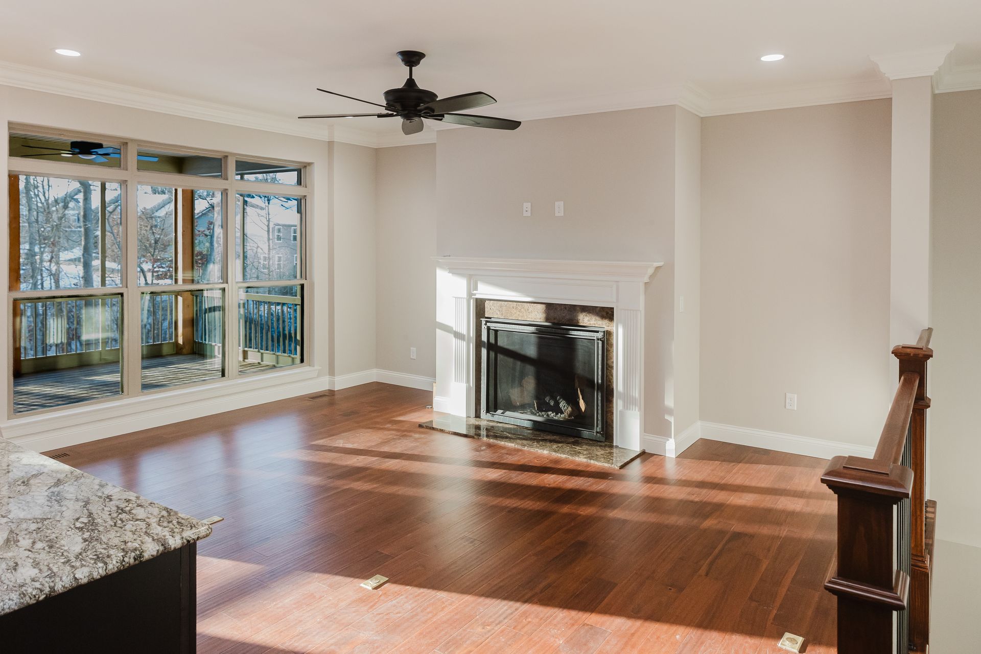 Living room of the Dean Martin model with fireplace, hardwood floors, large window, and ceiling fan.