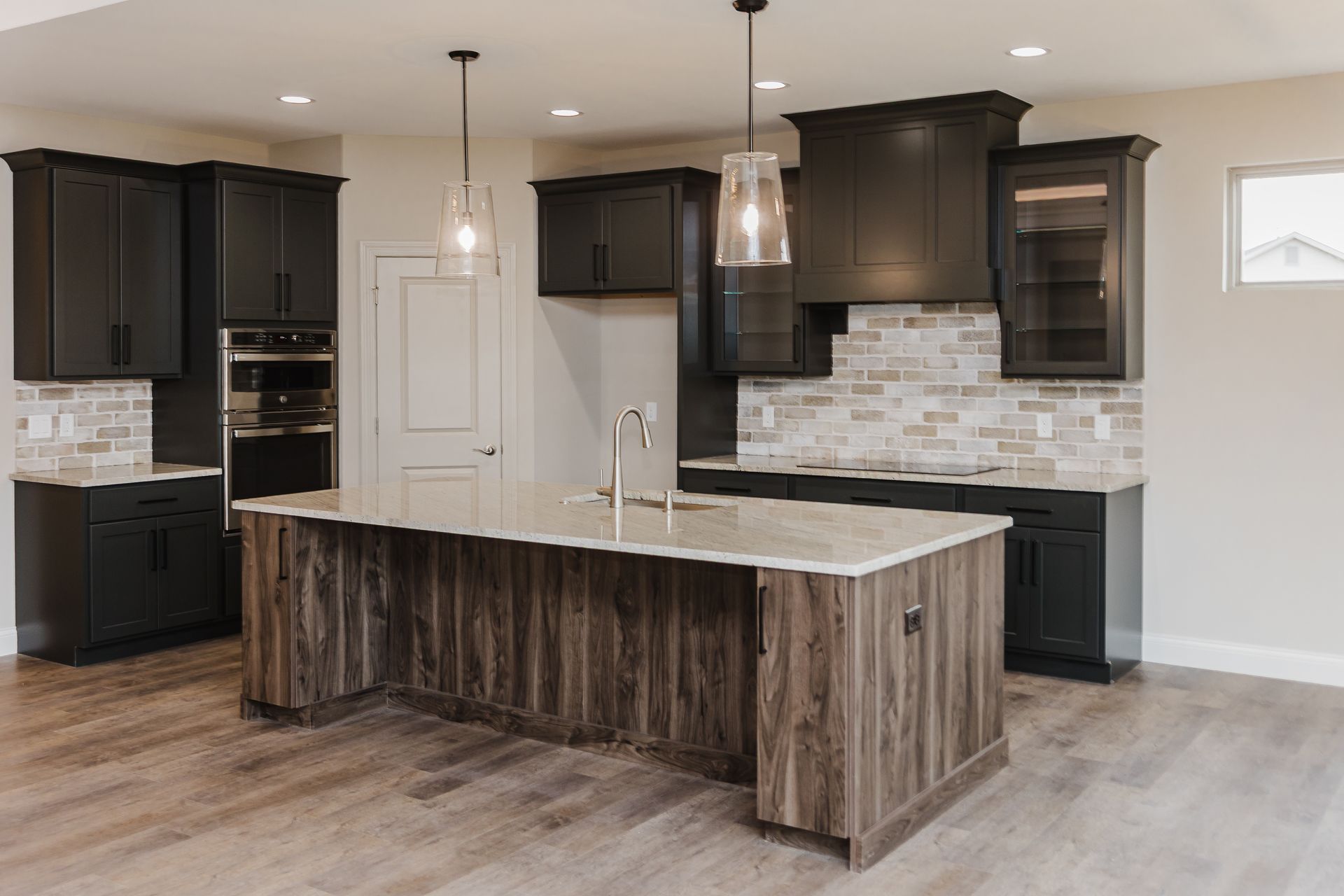 Modern kitchen of the Marilyn Monroe model with dark cabinets, wood island, light brick backsplash, and pendant lights.
